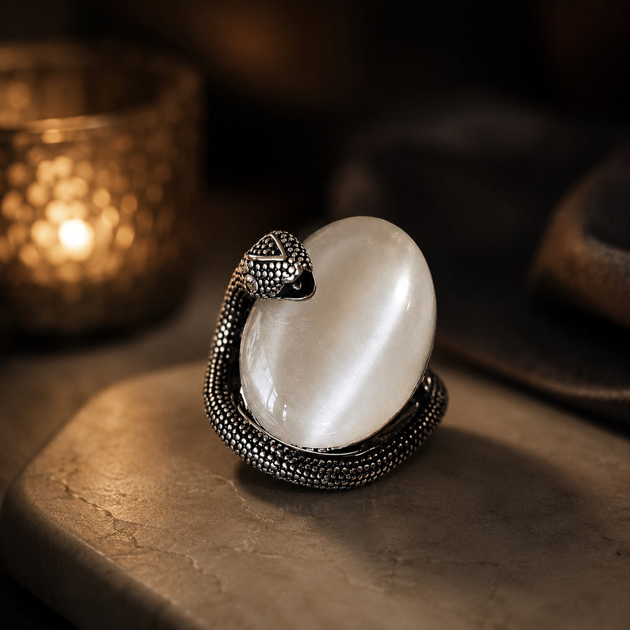 Cat’s Eye Stone Snake Ring featuring a coiled snake embracing an oval white cat’s eye gemstone in a warm ambient setting.