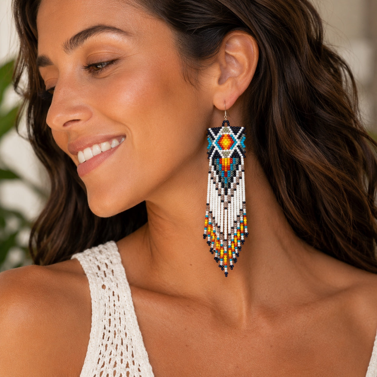 Close-up side view of woman wearing colorful Southwest beaded fringe earrings with long white tassels and geometric tribal design.