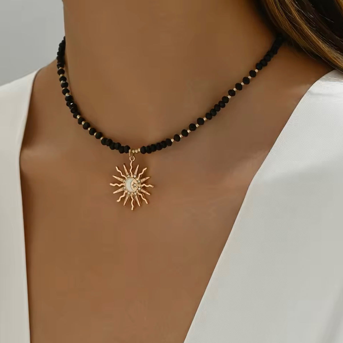 Black beaded sun pendant necklace with gold-tone spacer beads and a celestial sunburst charm worn with a white top.