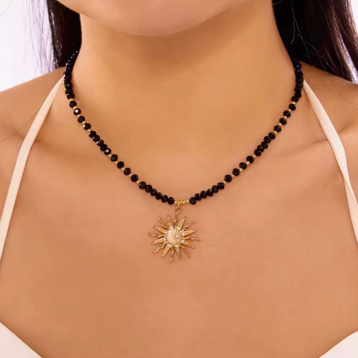 Black faceted beaded sun pendant necklace with gold accents and a celestial gold sun charm, shown worn.