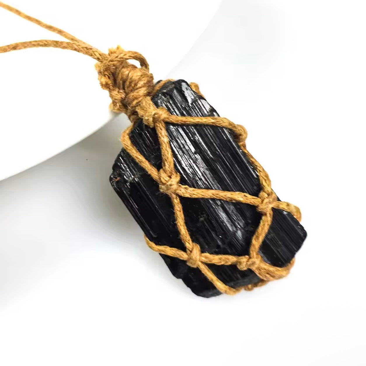 Close-up of raw black tourmaline crystal pendant wrapped in golden-brown cord.