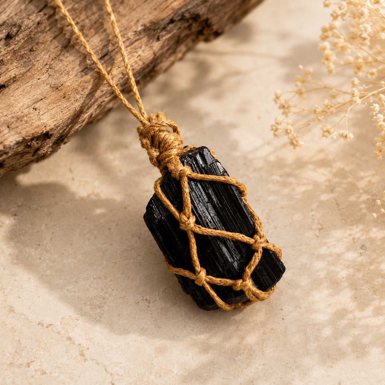 Black tourmaline pendant necklace with natural stone and golden-brown cord on a warm stone surface.