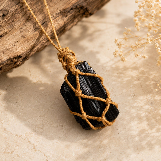 Black tourmaline pendant necklace with natural stone and golden-brown cord on a warm stone surface.