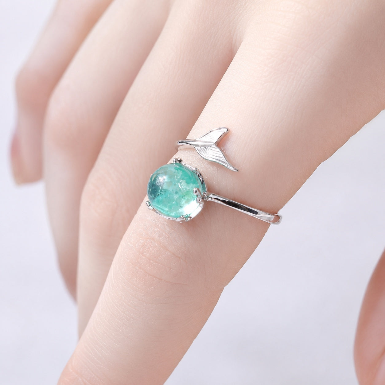 Blue Crystal Mermaid Ring worn on a finger, highlighting the shimmering blue crystal and delicate silver mermaid tail band.