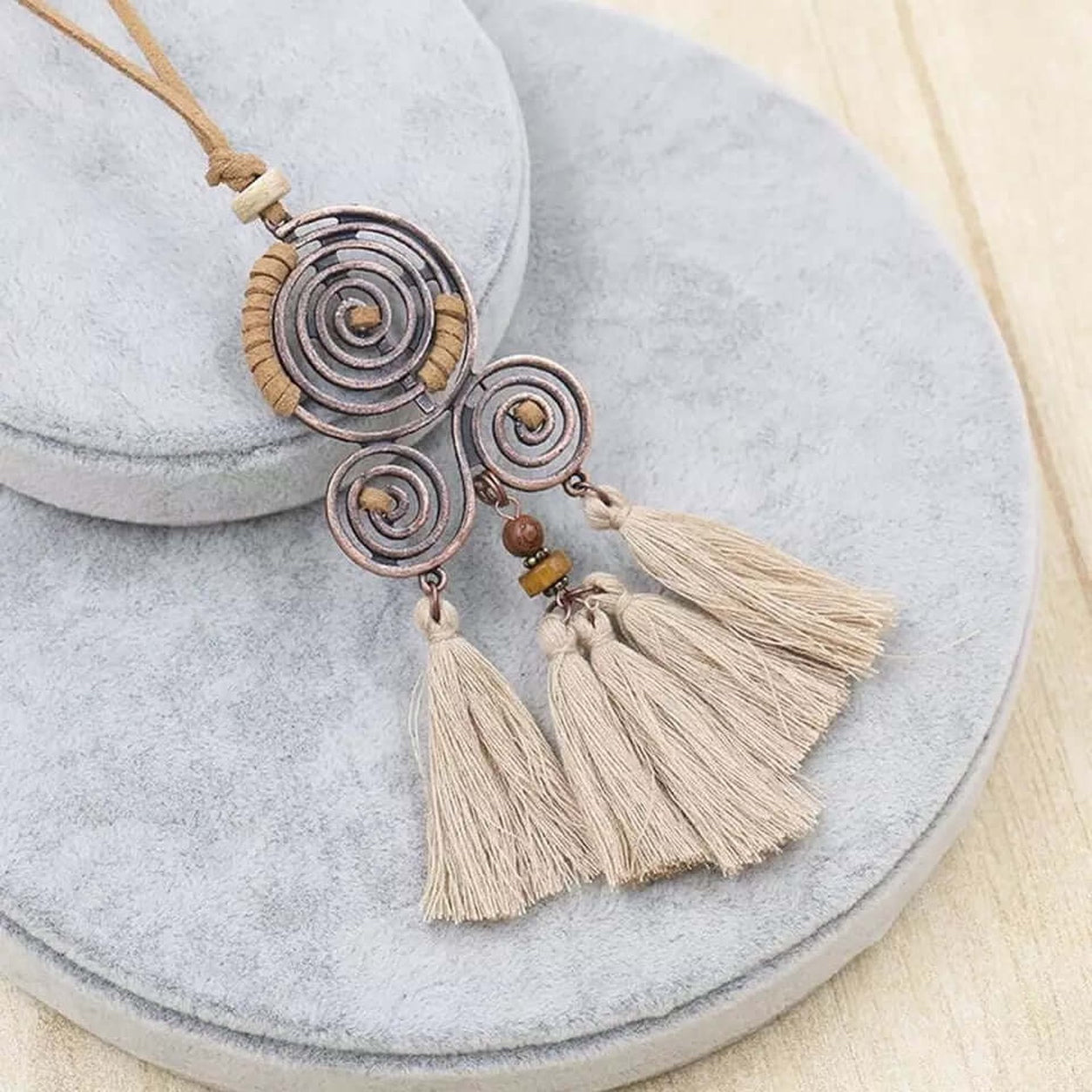 Close-up of the Boho Spiral Tassel Necklace with beige tassels, copper-tone spiral pendant, wooden bead accents, and faux suede cord.