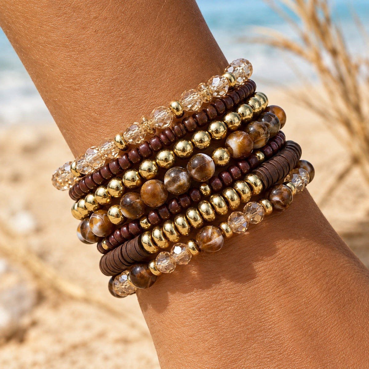 Brown, burgundy, champagne and gold-tone beaded stretch bracelets layered on a wrist in warm natural light.