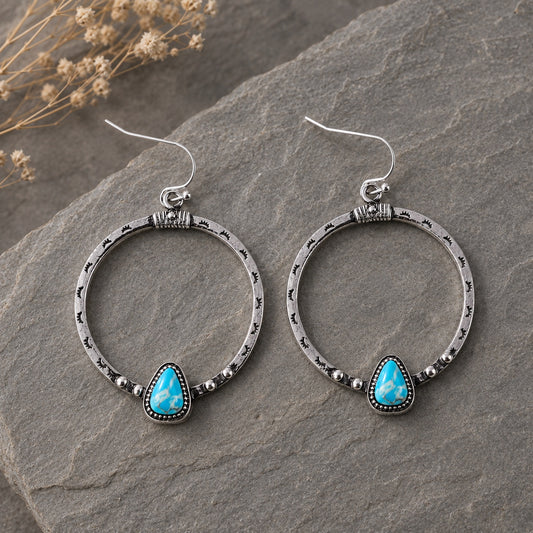 Canyonlands Hoop Earrings with engraved silver hoops and turquoise teardrop stones displayed on natural stone.