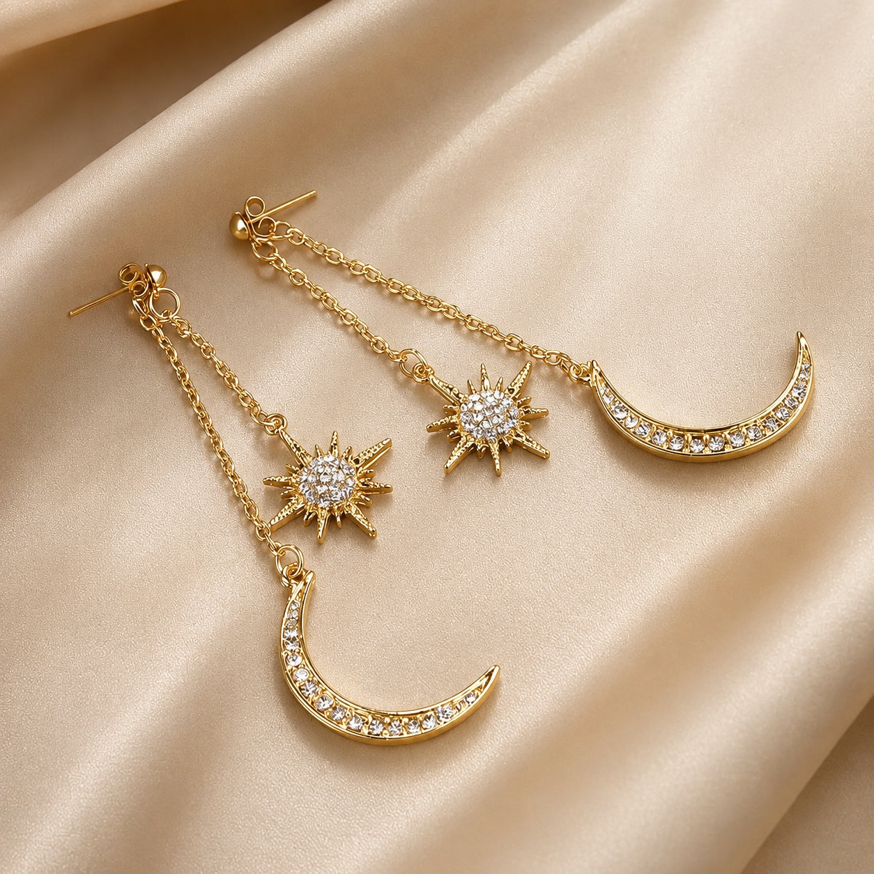 Gold Celestial Dangle Earrings featuring crystal crescent moon and star charms on a soft champagne satin background.