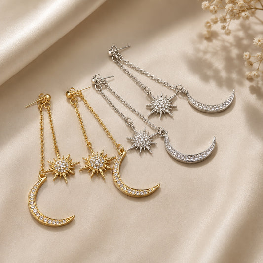 Celestial Dangle Earrings in gold and silver finishes with sparkling moon and star charms displayed on champagne satin.