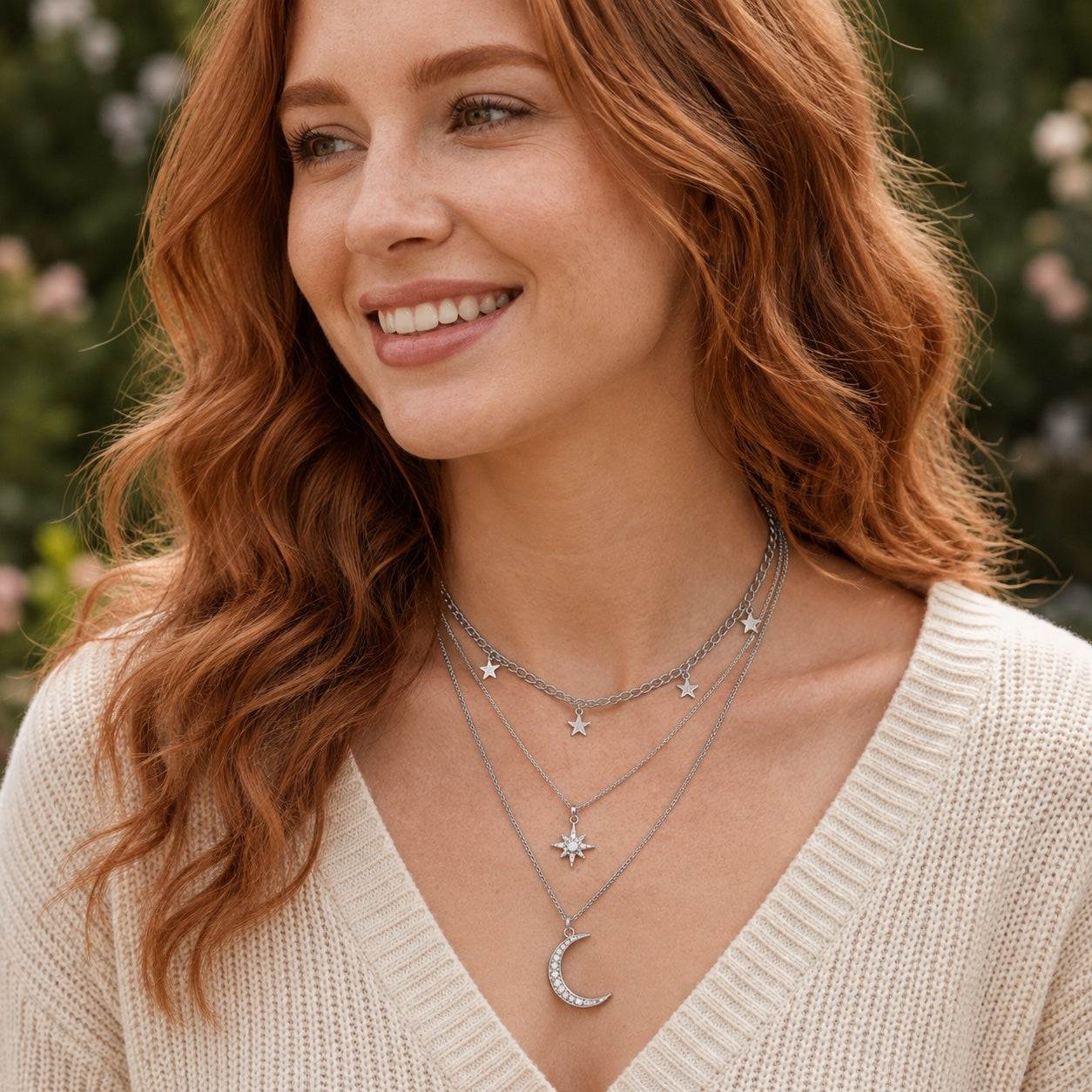 Silver celestial layered necklace with star charms, starburst pendant and crescent moon worn on a woman.