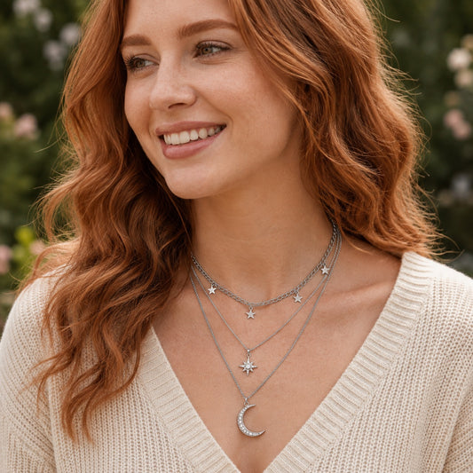 Silver celestial layered necklace with star charms, starburst pendant and crescent moon worn on a woman.