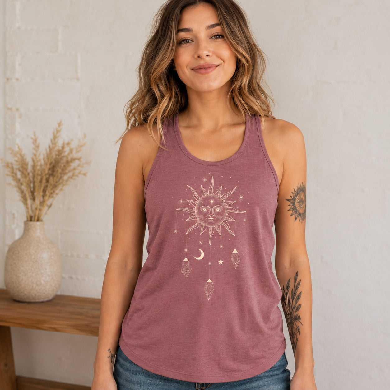 Woman wearing the Celestial Vibes Flowy Tank in heather mauve featuring a celestial sun, moon, stars, and crystal graphic.