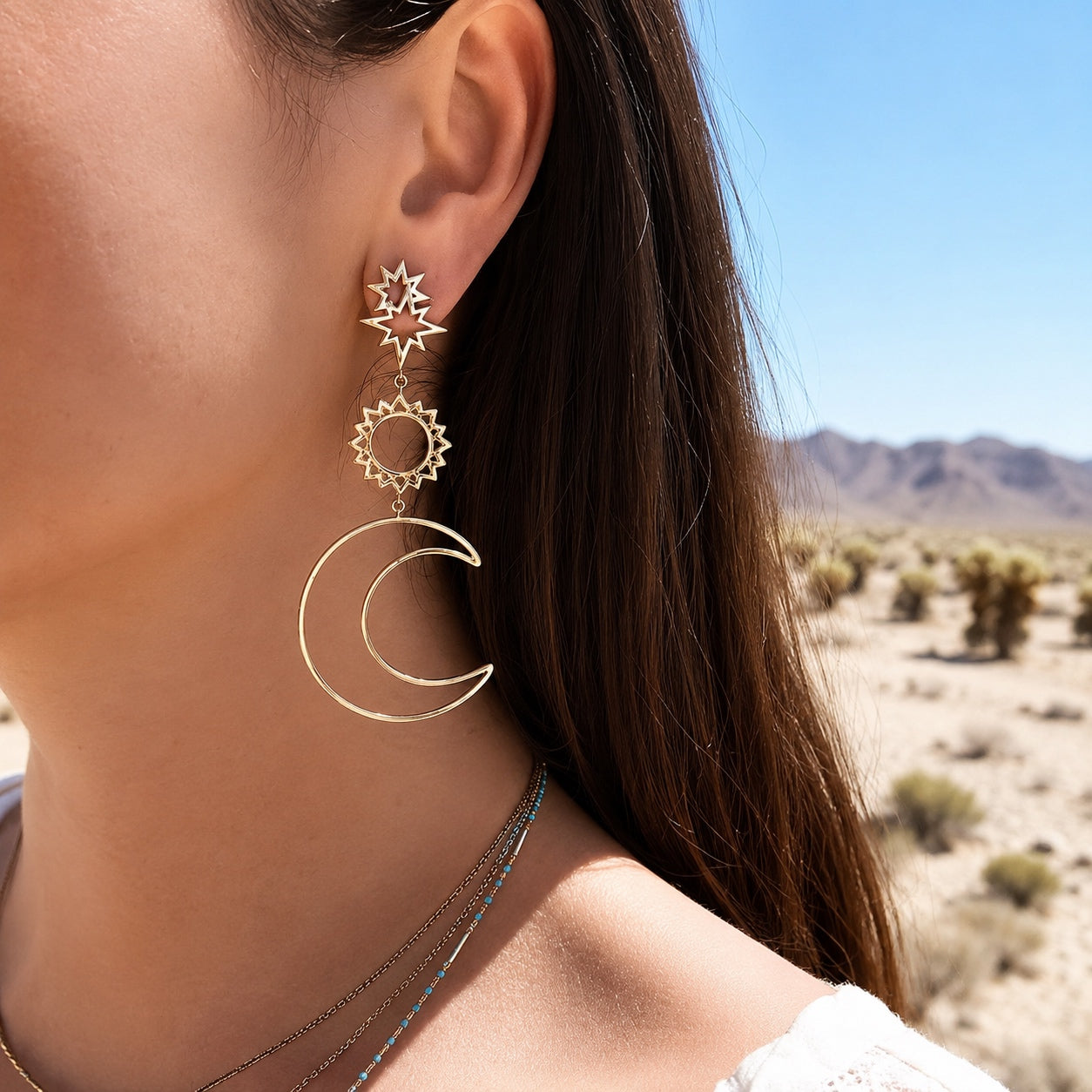 Celestial Wanderer Earrings in gold worn by a woman featuring celestial sun and crescent moon dangle earrings with boho style.