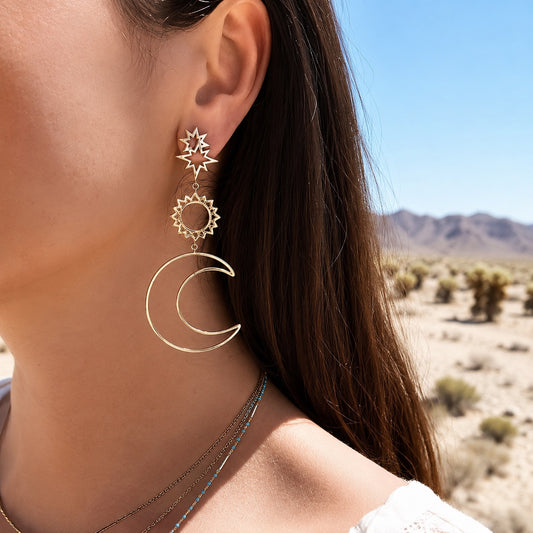 Celestial Wanderer Earrings in gold worn by a woman featuring celestial sun and crescent moon dangle earrings with boho style.