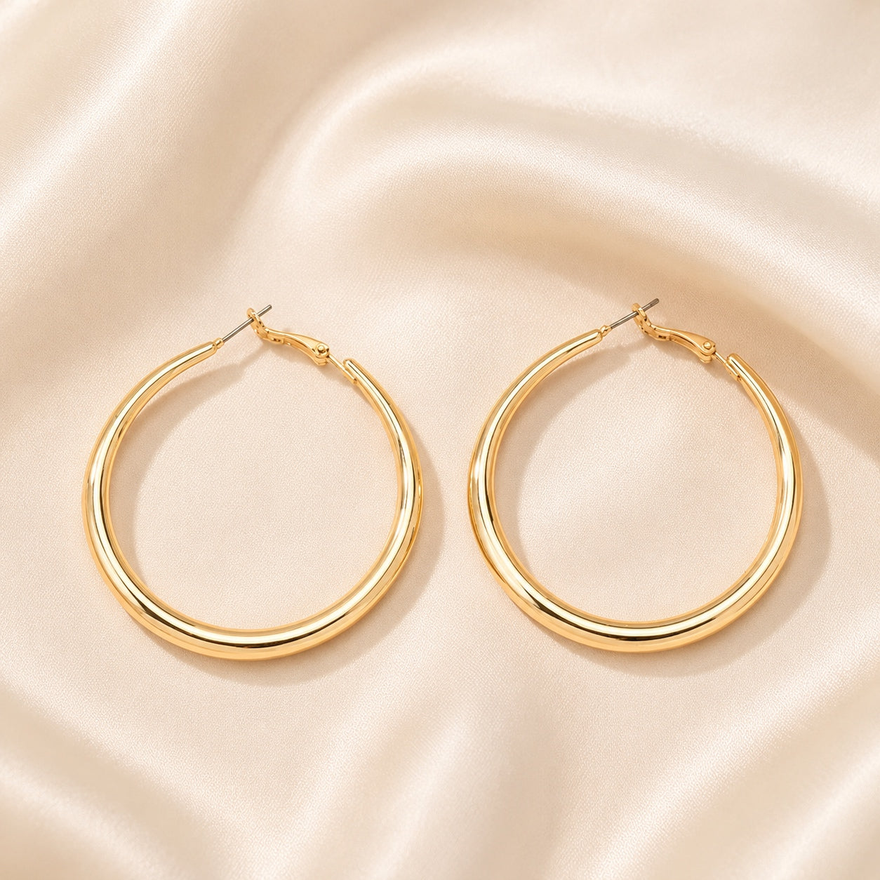 Classic Hoop Earrings in polished gold displayed on soft satin fabric, featuring a timeless minimalist hoop design.