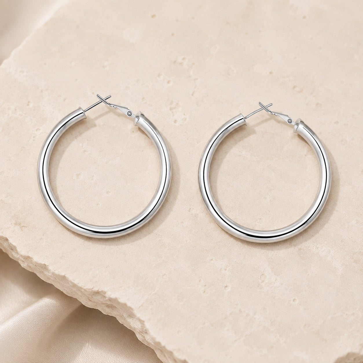 Classic Hoop Earrings in polished silver displayed on natural stone with a sleek minimalist hoop design.