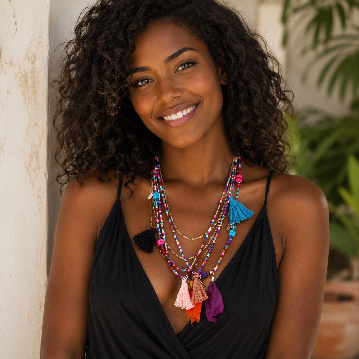 Woman wearing a colorful layered boho beaded necklace with tassels, vibrant feather pendants and mixed metal chains.