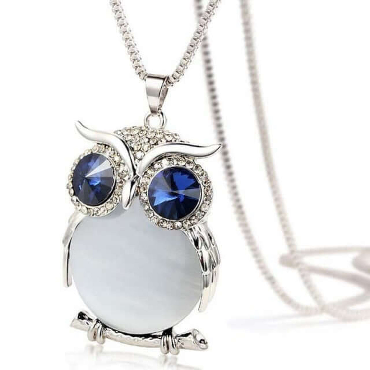 Crystal Owl Pendant Necklace in polished silver with deep blue crystal eyes and a luminous white stone, isolated on a clean white background.