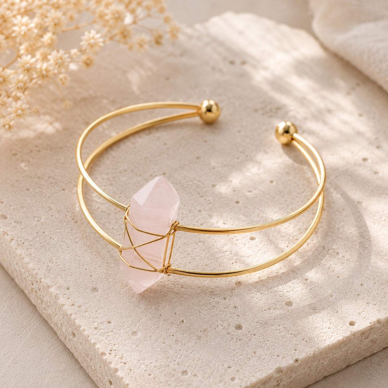 Close-up of a gold wire cuff bracelet with a rose quartz crystal centerpiece from the Crystal & Stone Bracelet Stack, displayed on a textured stone background.