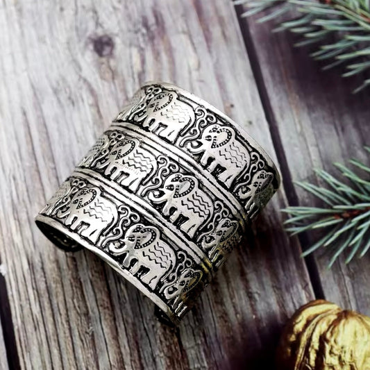 Elephant Cuff Bracelet in antique silver with engraved elephant pattern on a rustic wooden background.