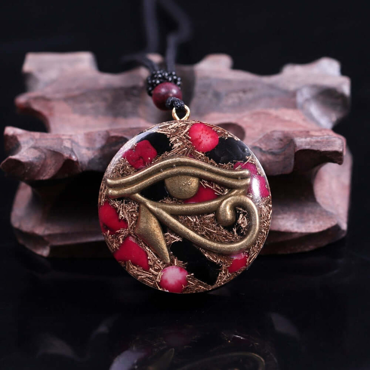 Eye Of Horus Pendant Necklace featuring a bronze Eye of Horus symbol with red coral accents in a handcrafted round resin pendant on black background.