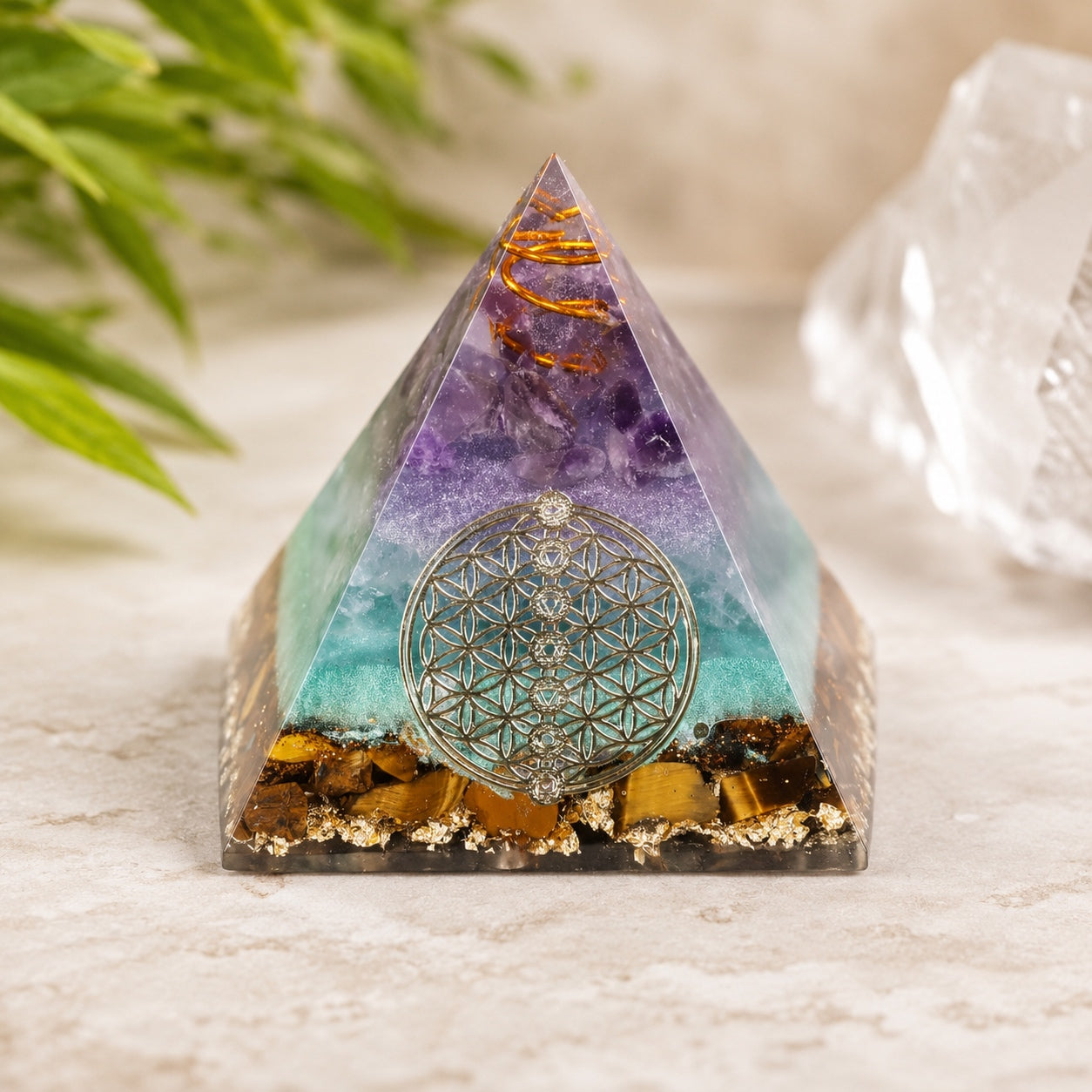 Flower of Life Crystal Pyramid displayed on a stone surface with crystal decor in a calming natural setting.