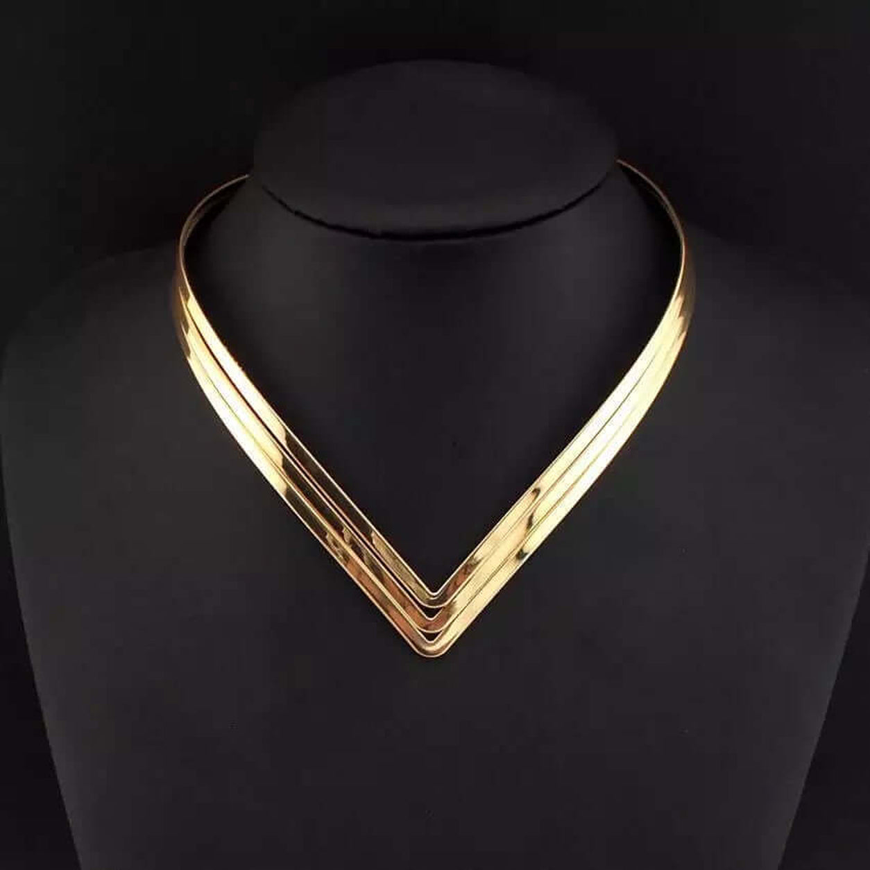 Gold Geometric Torque Collar Necklace displayed on a black jewelry bust showing its sculptural V silhouette.