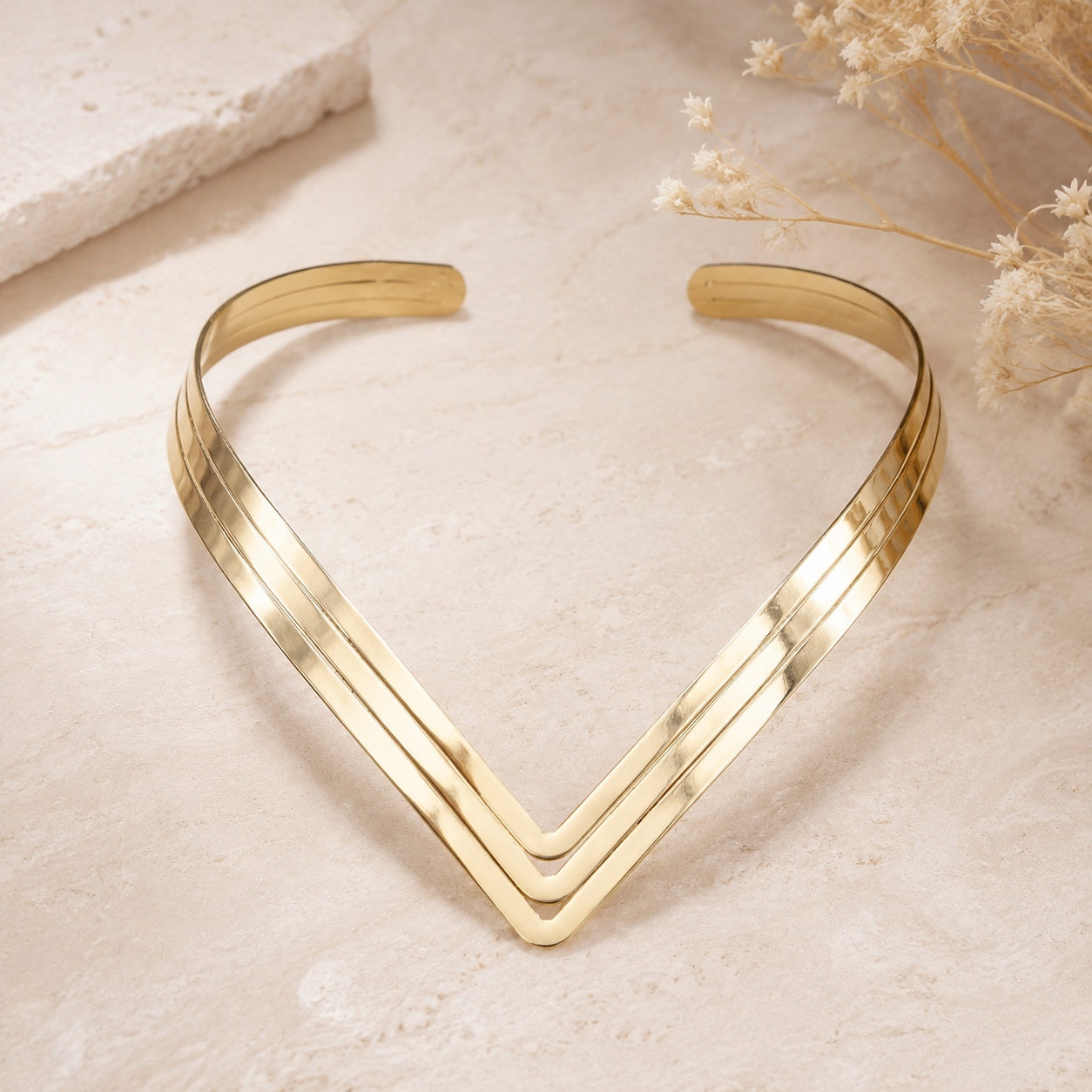 Gold Geometric Torque Collar Necklace shown on a neutral surface highlighting the open V-shaped collar design.