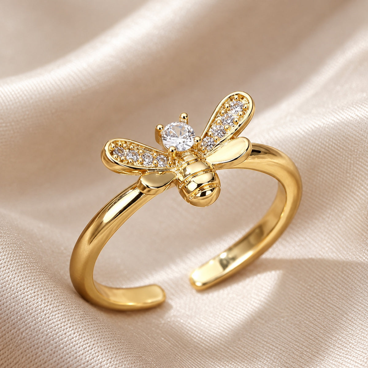 Gold bee ring with a clear crystal center and sparkling wings on champagne fabric