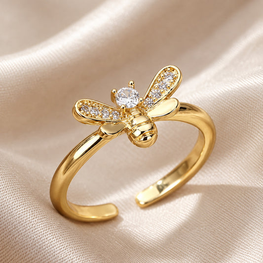 Gold bee ring with a clear crystal center and sparkling wings on champagne fabric