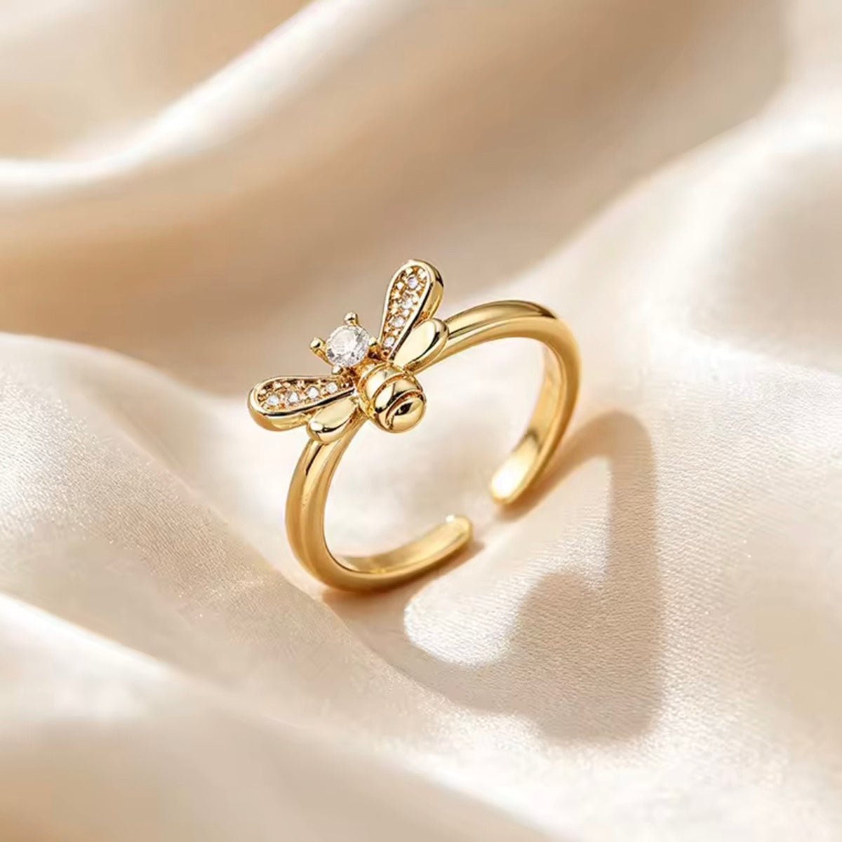Three-quarter view of a polished gold bee ring with a round clear stone and detailed wings