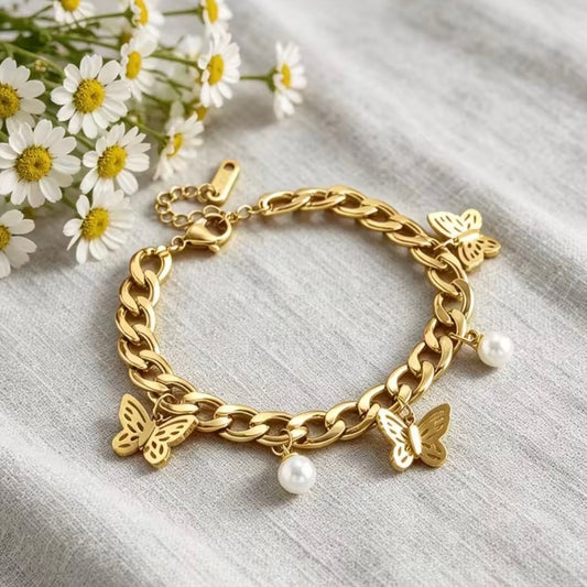 Gold butterfly charm bracelet with dangling pearl accents displayed on neutral linen beside white daisies.