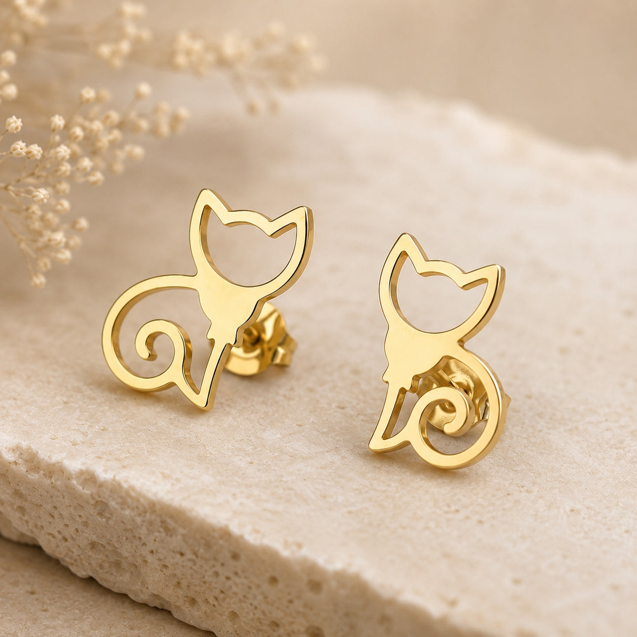 Close-up of gold cat stud earrings featuring an elegant minimalist cat silhouette on a neutral stone display.
