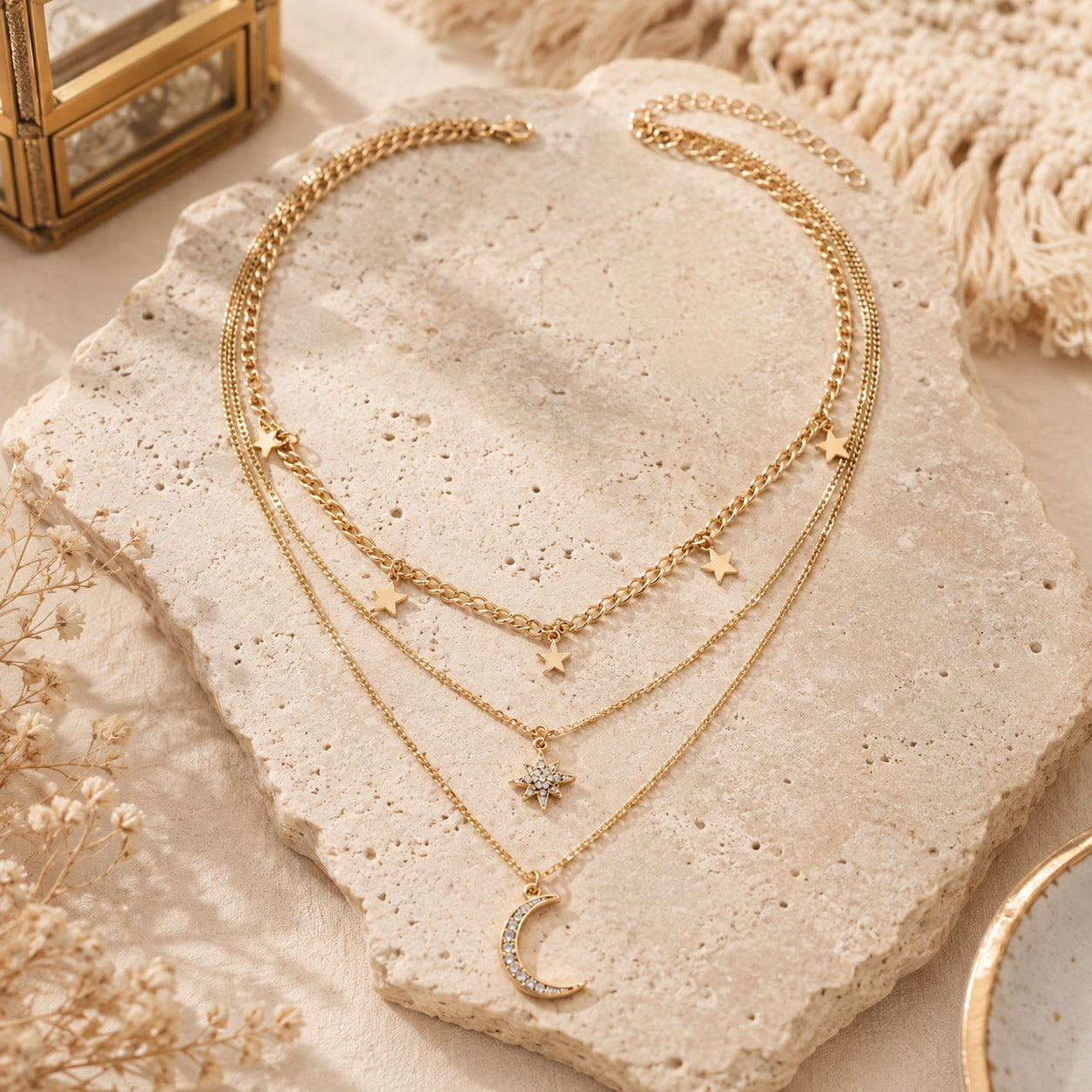 Gold layered necklace with star charms, starburst pendant and crescent moon displayed on a stone surface.