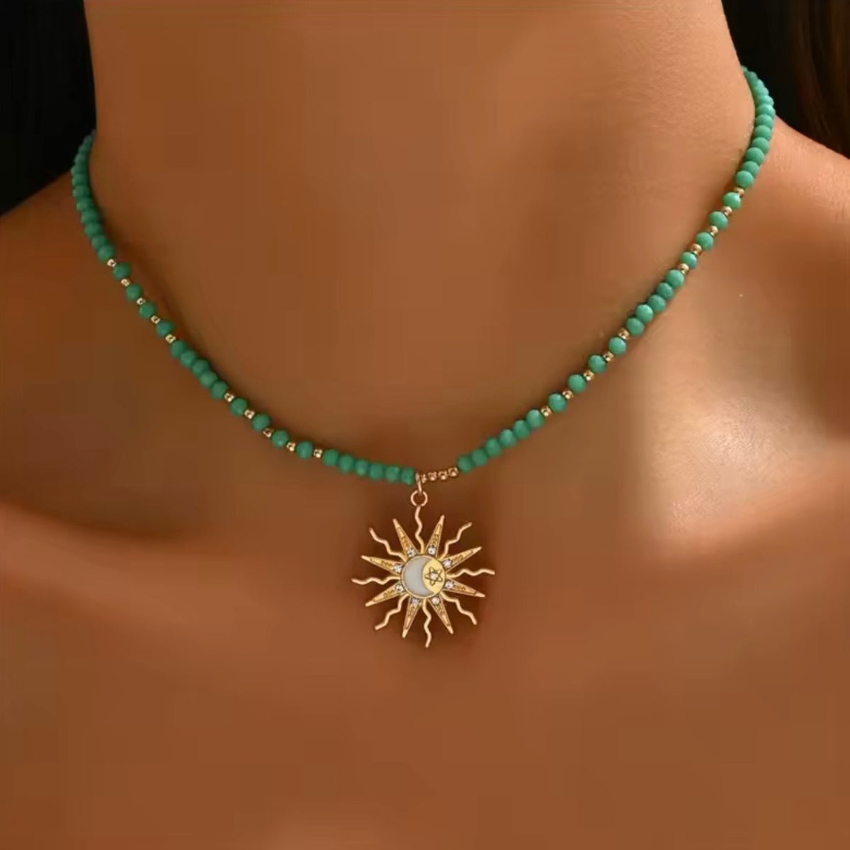 Turquoise-green beaded sun necklace with gold accents and a gold celestial pendant, shown worn around the neck.