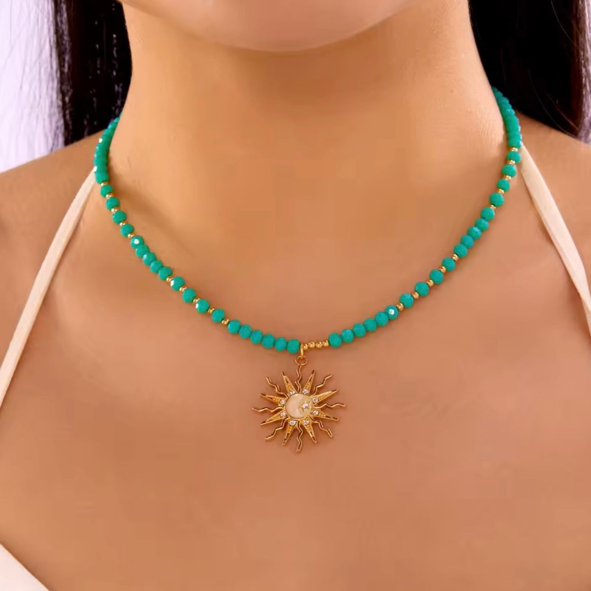 Green beaded sun pendant necklace with gold-tone spacer beads and a celestial sunburst charm worn at the neckline.