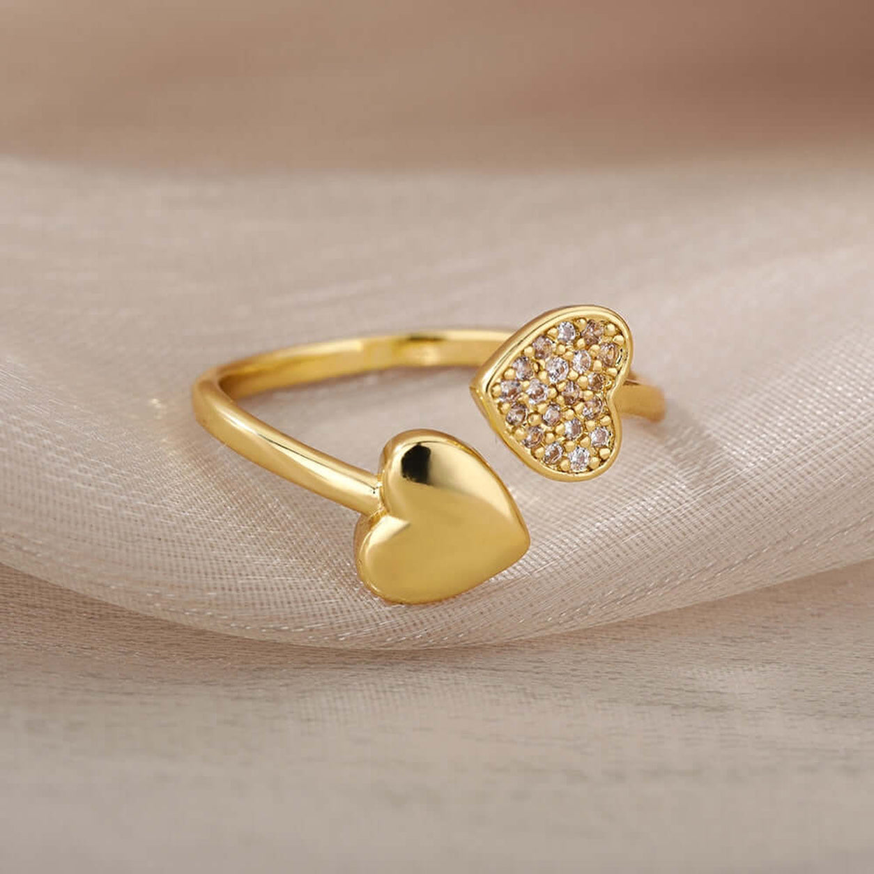 Adjustable Hearts Of Gold Ring displayed on sheer fabric, featuring two open hearts with crystals.