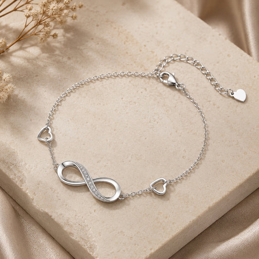 Infinity Bracelet displayed on a beige stone slab with delicate floral accents, featuring a polished infinity charm and heart details.
