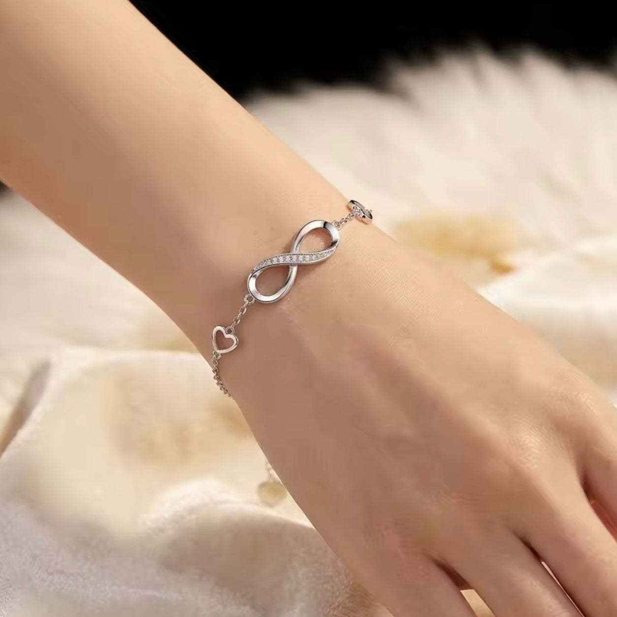 Woman wearing the Infinity Bracelet featuring a silver infinity symbol with crystal accents and delicate heart charms.