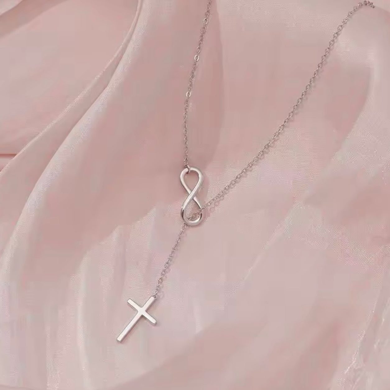 Sterling silver Infinity Cross Necklace arranged on blush fabric, showcasing the elegant infinity symbol and cross pendant.