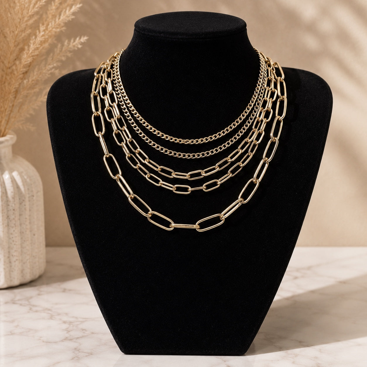 Layered Chains Necklace in gold featuring four layered paperclip and curb chains displayed on a jewelry stand.