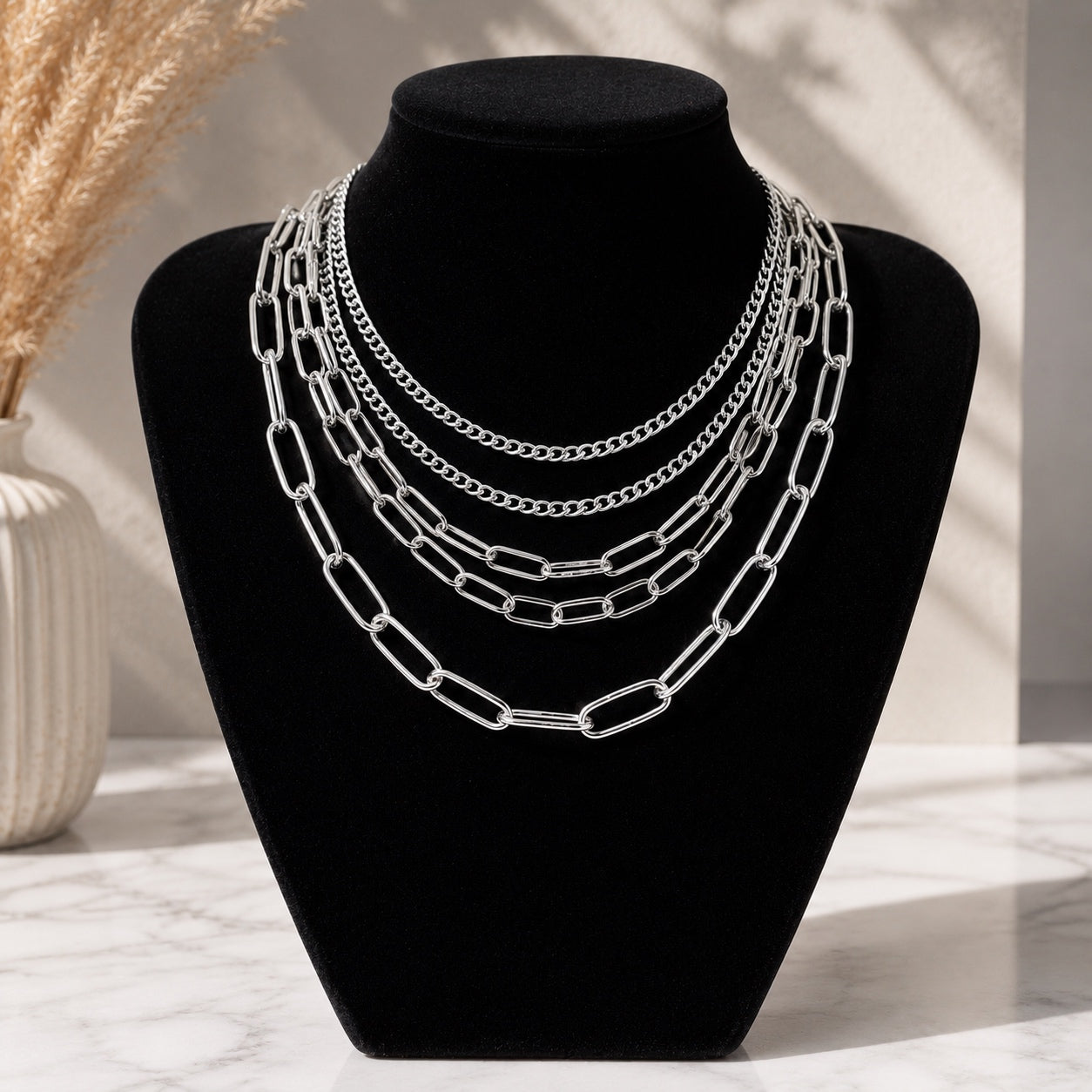 Layered Chains Necklace displayed on a black jewelry bust featuring four silver paperclip and curb chains.