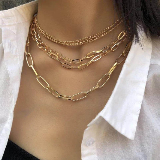 Woman wearing the Layered Chains Necklace with four silver paperclip and curb chains styled with an open-collar shirt.