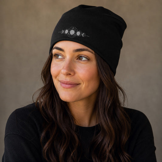 Woman wearing the black Moon Magic Beanie Hat featuring a celestial moon phase design on the front in a cozy lifestyle setting.