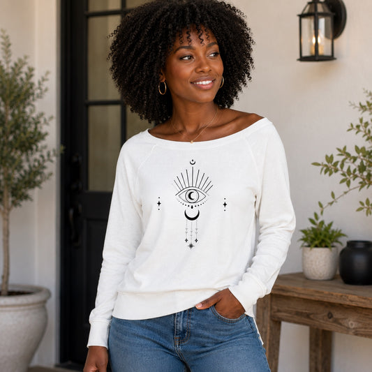 Woman wearing the white Moongazer Wide Neck Sweatshirt with celestial moon and eye graphic in a modern outdoor setting.