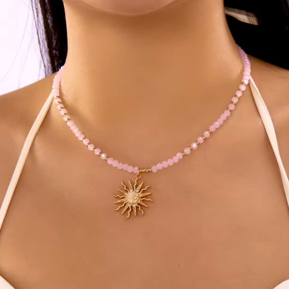 Pink beaded necklace with gold-tone accents and a celestial sunburst pendant featuring a crescent moon.