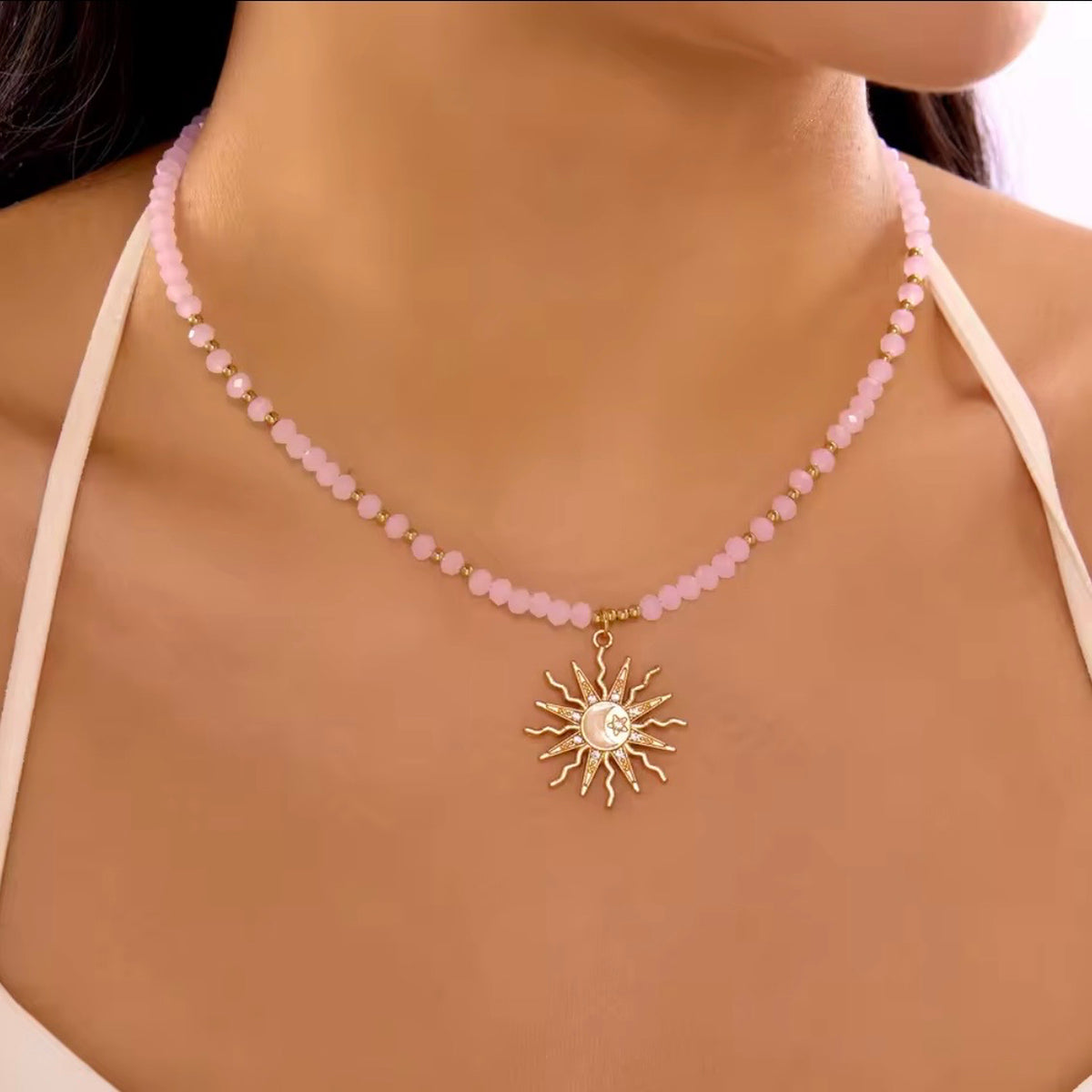 Pink faceted beaded necklace with gold accents and a celestial sun pendant, modeled on the neck.
