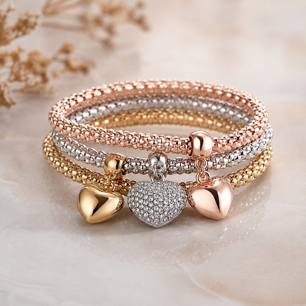 Queen Of Hearts Charm Bracelet Set in rose gold, silver and gold with crystal heart charm displayed on a marble surface.