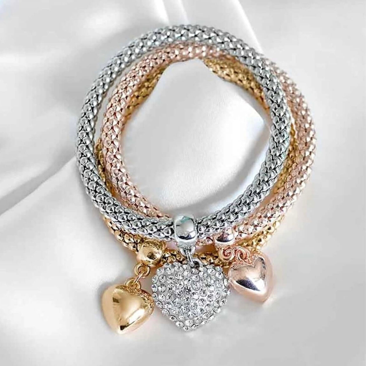 Queen Of Hearts Charm Bracelet Set with rose gold, silver and gold stretch bracelets and heart charms on white fabric.