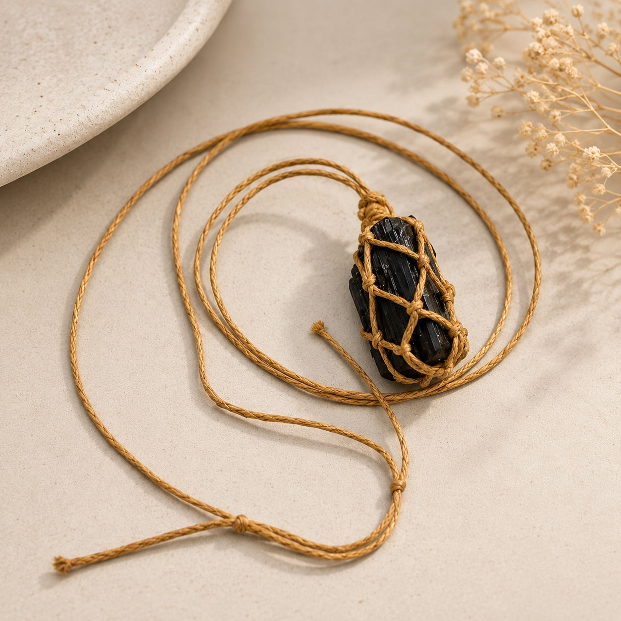 Raw black tourmaline pendant necklace with hand-wrapped cord arranged on a neutral stone surface.